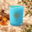 Mahonie Amber Candle, turquoise glass, on pale natural stone.