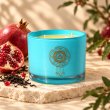 Mahonie Black Tea & Pomegranate Candle, turquoise glass, on pale natural stone.