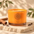 Mahonie Cinnamon & Clove Candle, orange glass, on pale natural stone.