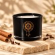 Mahonie Cinnamon & Clove Candle, black glass, on pale natural stone.