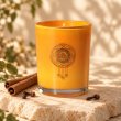 Mahonie Cinnamon Clove Candle, orange glass, on pale natural stone.