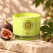 Mahonie Fig & Moss Candle, yellow-green glass, on pale natural stone.