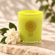 Mahonie Gardenia Candle, yellow-green glass, on pale natural stone.