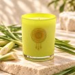 Mahonie Lemongrass Candle, yellow-green glass, on pale natural stone.