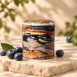 Mahonie Métallique : Blissful Blueberry Candle, multicolour patterned vessel, on pale natural stone.