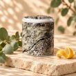 Mahonie Métallique : Citric Eucalyptus Candle, grey patterned vessel, on pale natural stone.