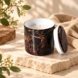 Mahonie Métallique : Midnight Musk Candle, dark marble-pattern vessel, on pale natural stone.