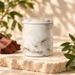 Mahonie Métallique : Noble Rosewood Candle, pale marble-pattern vessel, on pale natural stone.