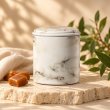 Mahonie Métallique : Silk & Satin Caramel Candle, pale marble-pattern vessel, on pale natural stone.