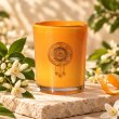 Mahonie Orange Blossom Candle, orange glass, on pale natural stone.