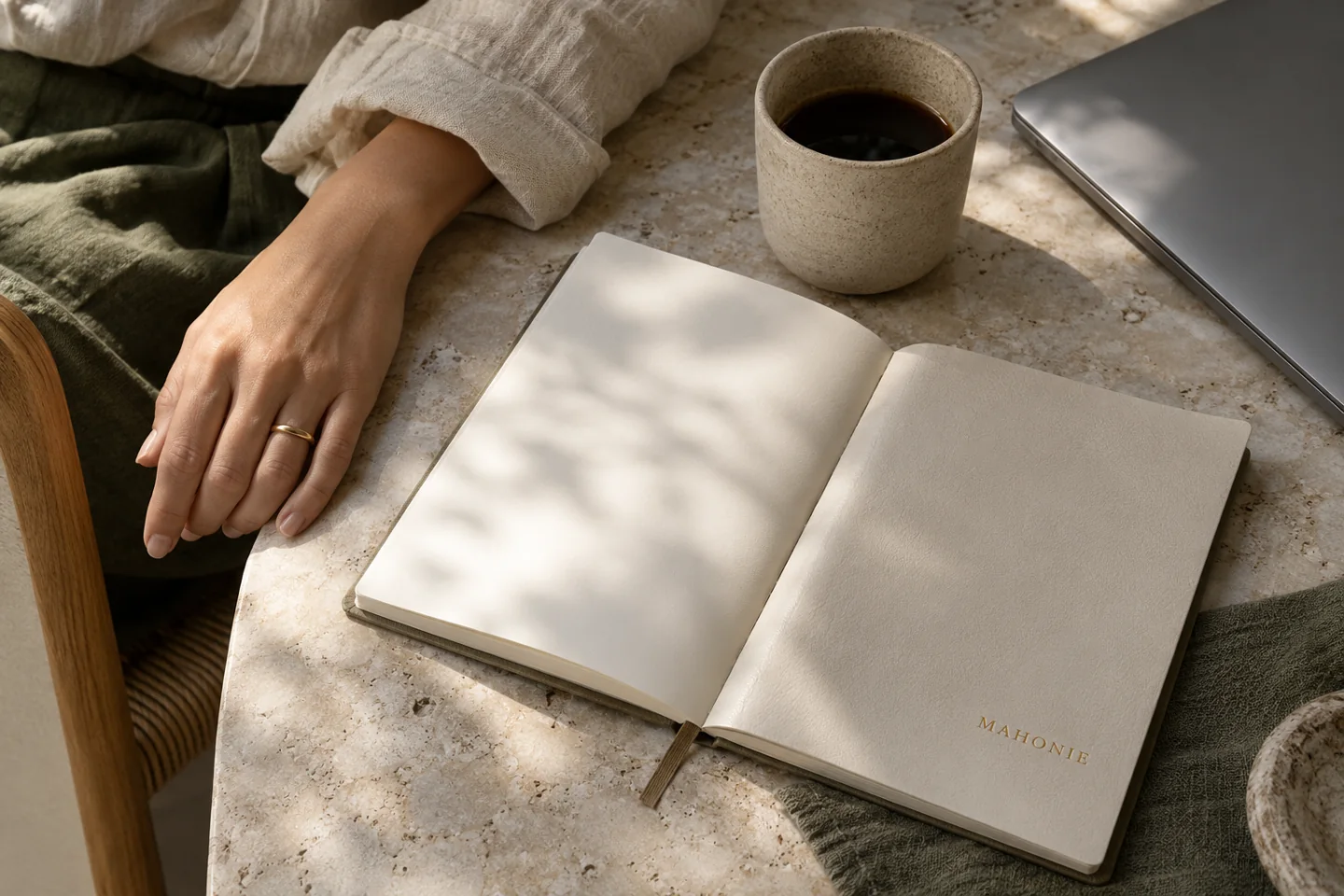 A relaxed hand beside a Mahonie notebook and ceramic cup on a stone desk