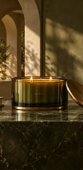 Olive glass Mahonie candle with its lid on a dark stone table